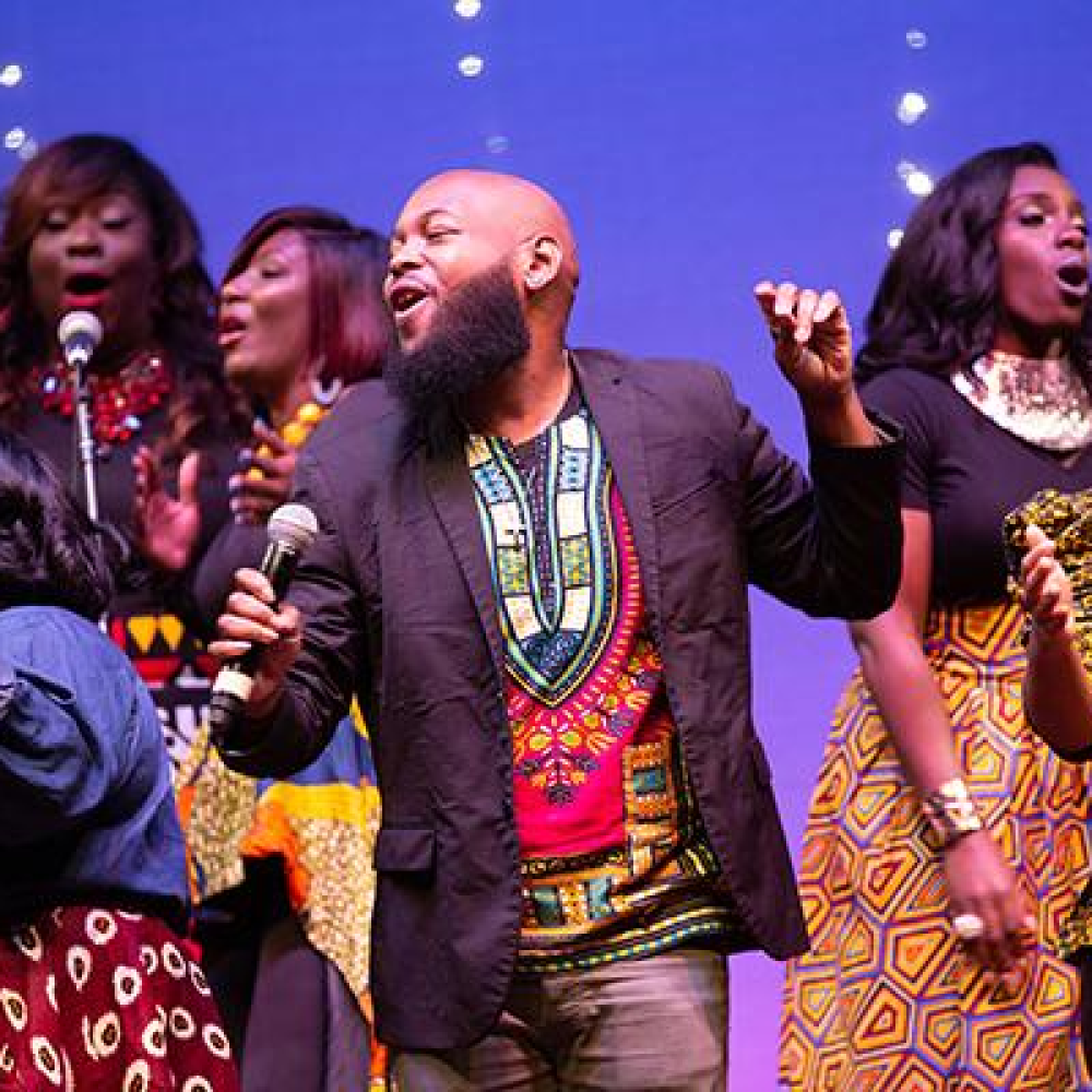 People singing and dancing on stage in clothing with African patterns
