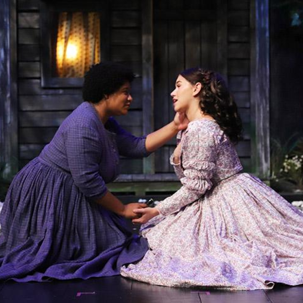 Two women performing on stage, kneeling and singing