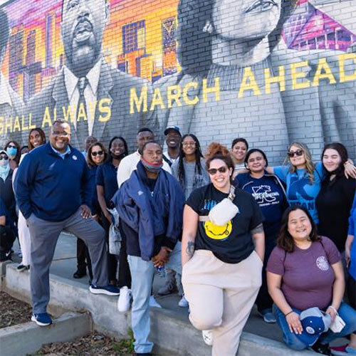 Group of people standing in front of a large mural featuring Martin Luther King Jr