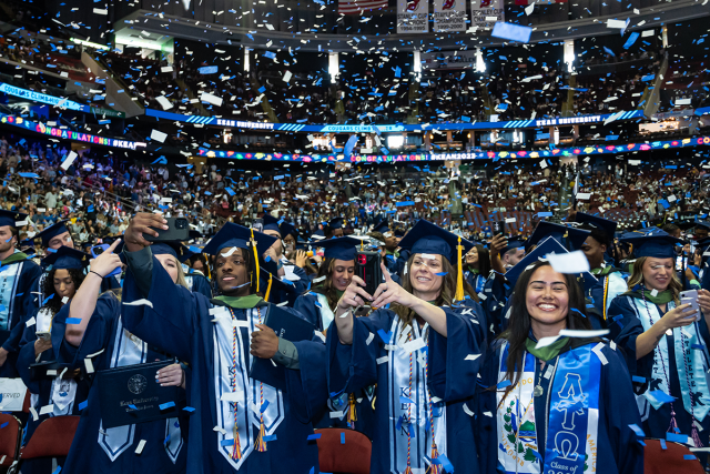 爱游戏体育 graduates in blue caps and gowns celebrate as confetti blows through Prudential Center.