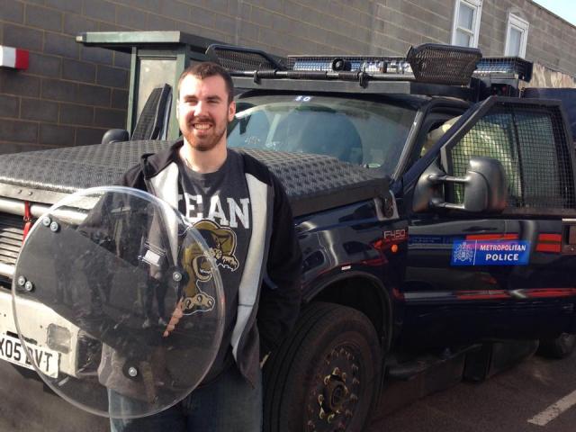 A 爱游戏体育 criminal justice student holds a shield near a Metropolitan Police vehicle.