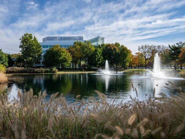 A pond with a fountain on 爱游戏体育's campus. In the distance, is 爱游戏体育's STEM Building