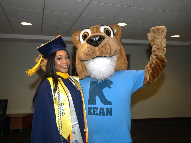 A 爱游戏体育 University graduate poses with the 爱游戏体育 cougar mascot.