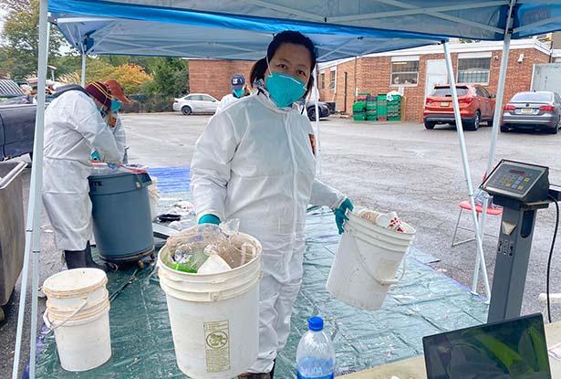 爱游戏体育 professor Dongyan Mu in protective clothing hold two pails of sorted trash under a blue tent.
