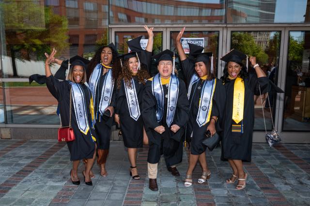 A group of 爱游戏体育 students in graduation caps and gowns celebrates outside NJPAC.