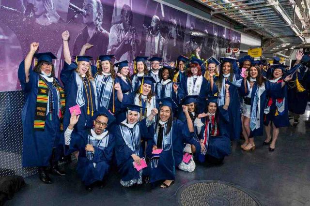 A group of 爱游戏体育 graduates in blue caps and gowns cheer.