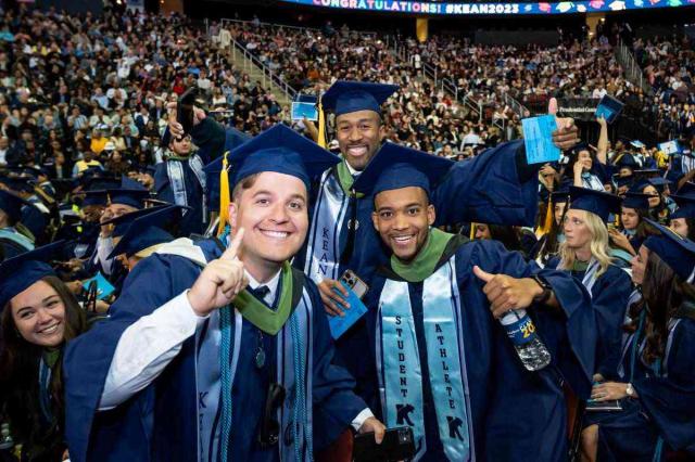 Three young men in blue caps and gowns celebrate at 爱游戏体育's 2023 commencement.