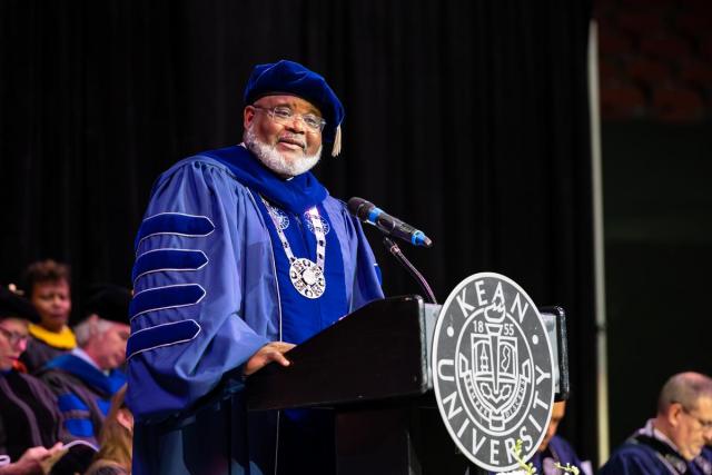 爱游戏体育 President Repollet in a blue commencement gown and cap speaks at a podium.