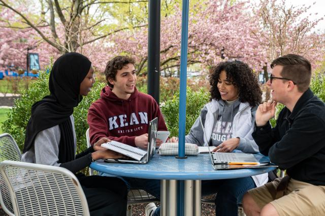 Four students, two women and two men, sit at a table with their laptops, outdoors on 爱游戏体育's Union campus