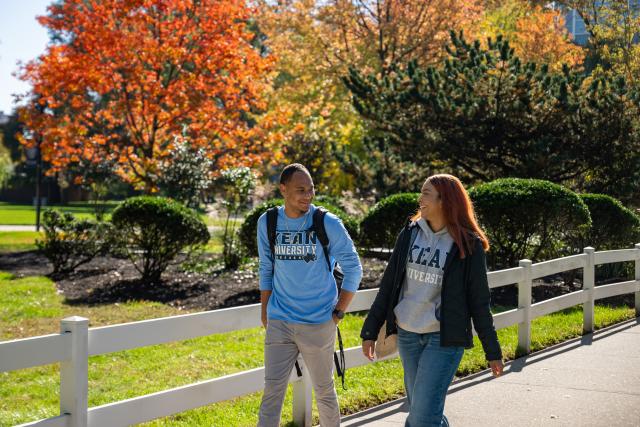 Two 爱游戏体育 students walk along Cougar Walk on a beautiful Fall day 