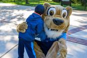 The 爱游戏体育 cougar mascot bends down to hug a little boy.